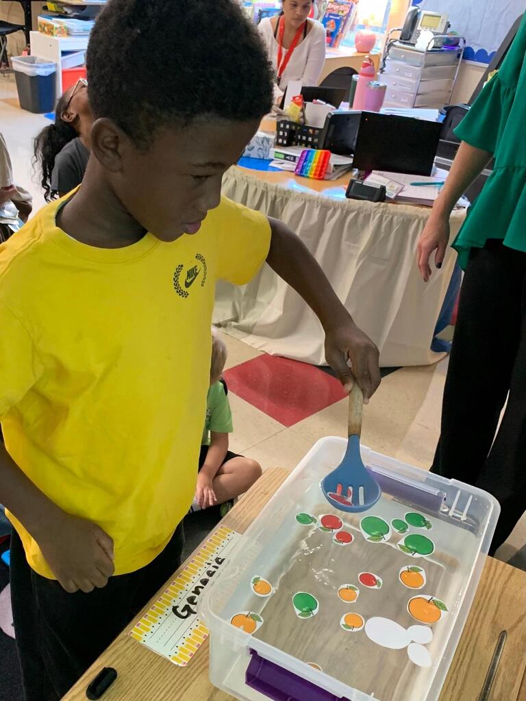 student holding a spoon in water with apples