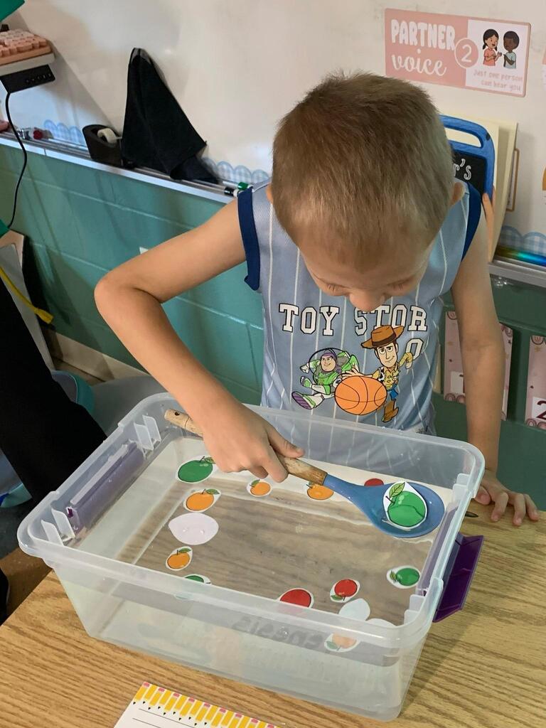 student holding a spoon in water with apples