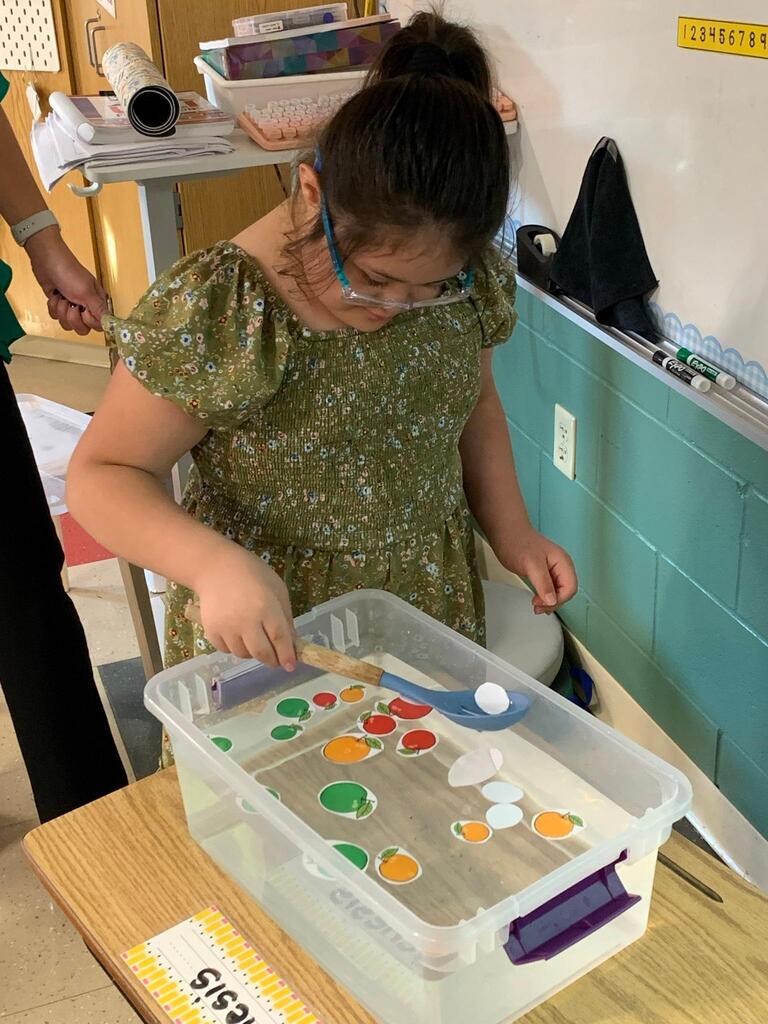 student holding a spoon in water with apples