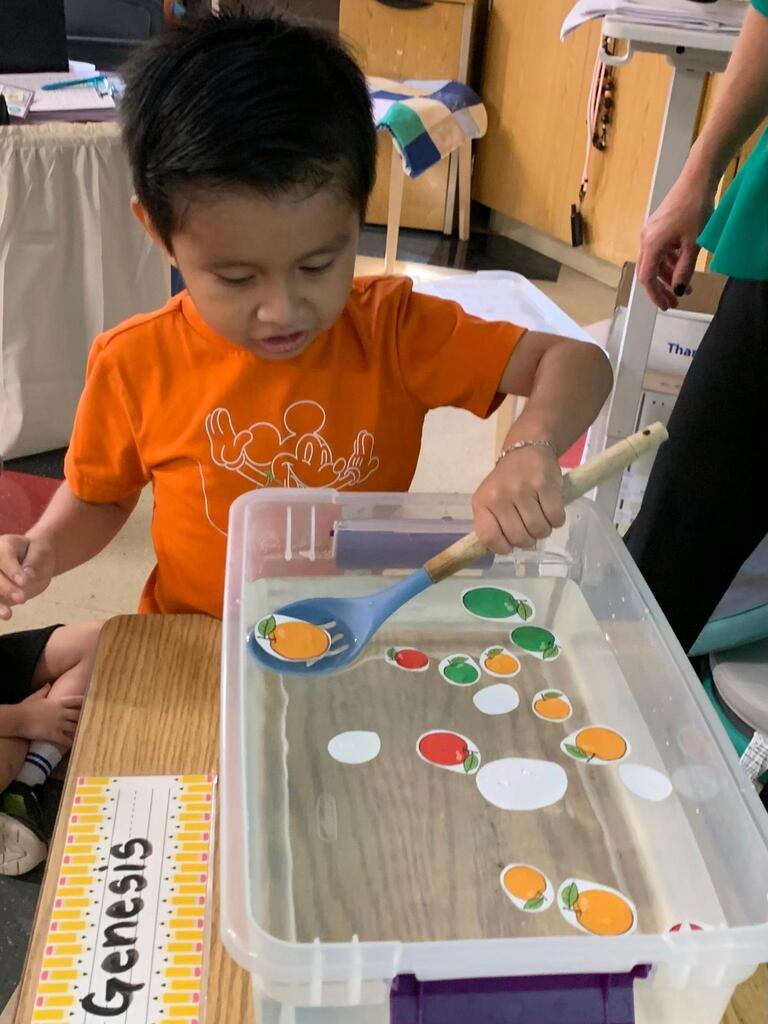 student holding a spoon in water with apples