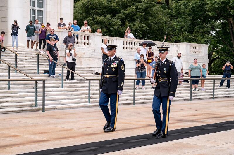 Officers standing among the marble colonnades of the Memorial Amphitheater as the wreath — bearing the department's name in red, white, and blue — was carried forward and placed at the Tomb by the U.S. Army's elite Tomb Guard sentinels.