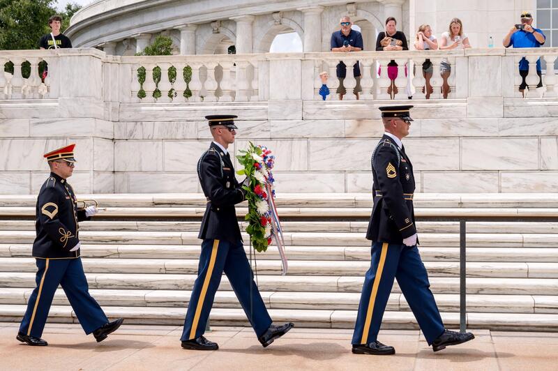 Three uniformed officers walking by the columns, with the middle one carrying the wreath of honor.