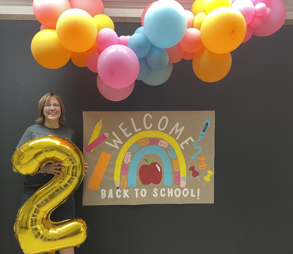 Picture of retiring 2nd grade teacher, Jeanette Scott holding an inflatable #2 and standing under balloons