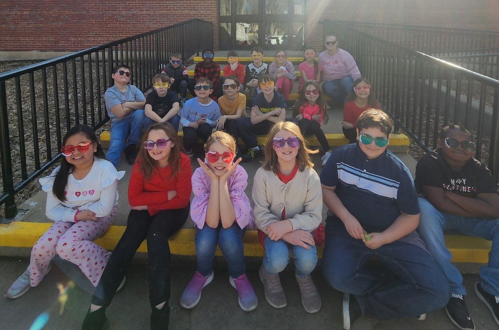 Students in Mrs. Quanstrom's class sitting on steps outside of Lincoln school, all wearing  heart shaped sunglasses