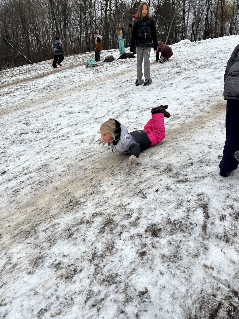 Girl sliding down snowy hill on her stomach