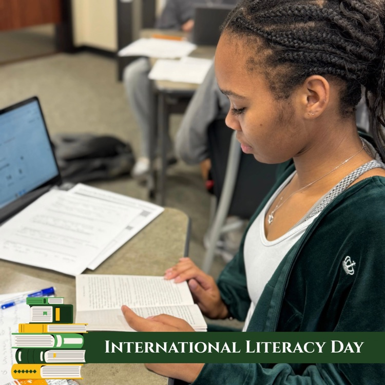 Junior Aaliyah Caldwell reads Of Mice and Men during class. Graphic banner says International Literacy Day with a stack of books in the bottom left corner. 