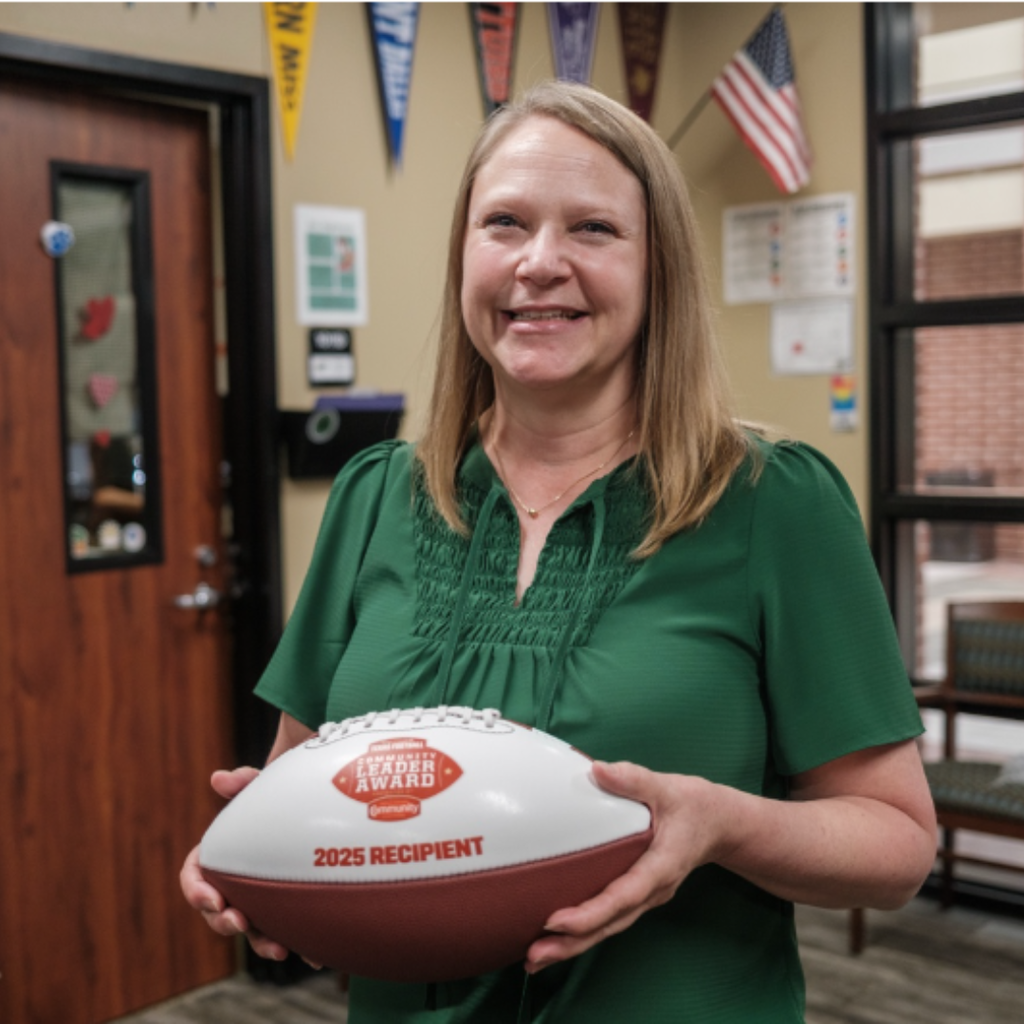 Julie Cooper smiles while holding her 2025 Community Leader Award football inside Prosper High School.