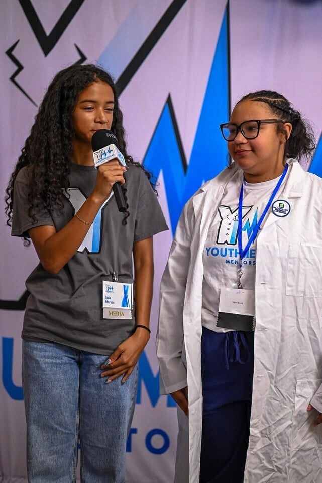 Lady speaking in a microphone with a scrub Club member