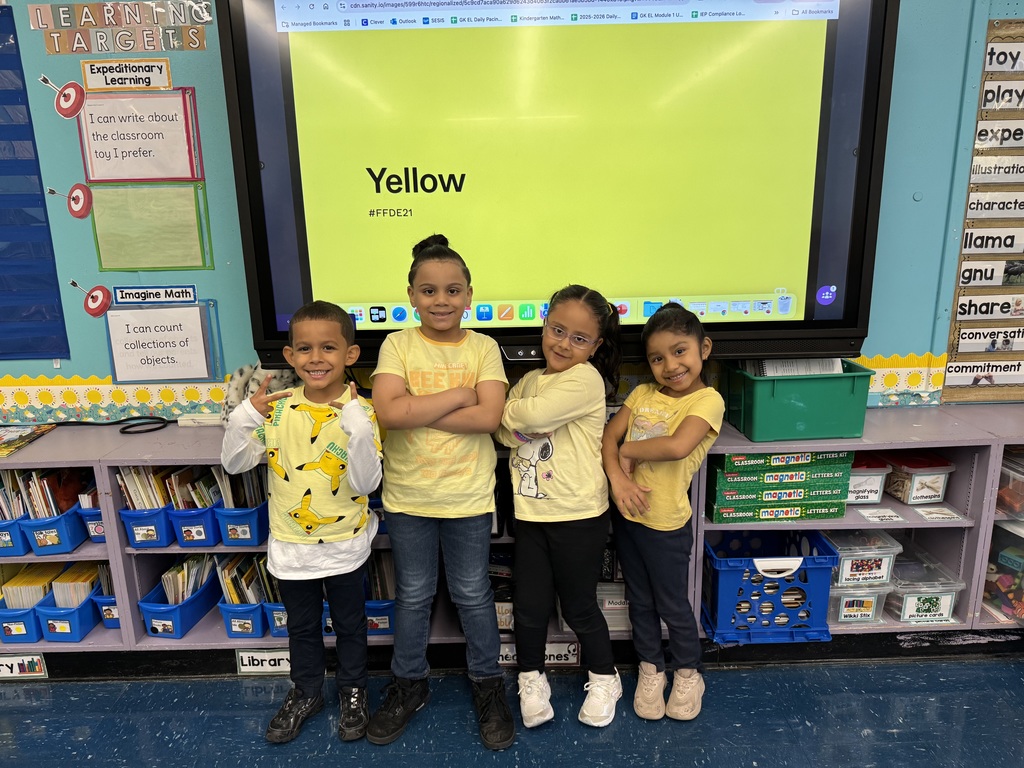 Four students wearing yellow shirts and posing in front of a big yellow screen showing the word "yellow"