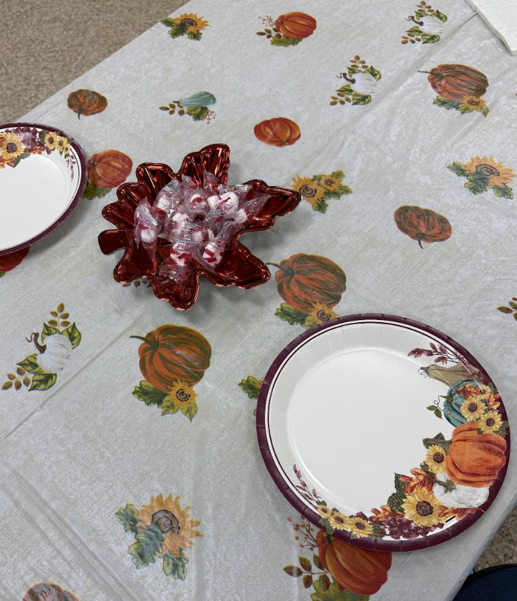 A fall-themed table setup with paper plates featuring pumpkins and flowers, and a red leaf-shaped bowl filled with mints in the center.