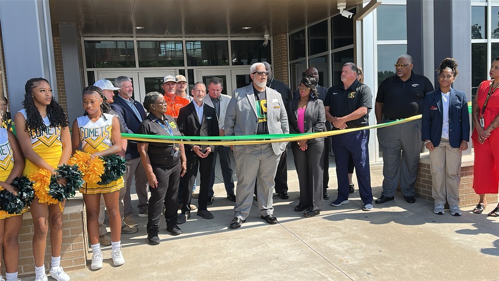 Group of cheerleaders, PCSSD administrators and others stand behind a ribbon before the ribbon-cutting ceremony