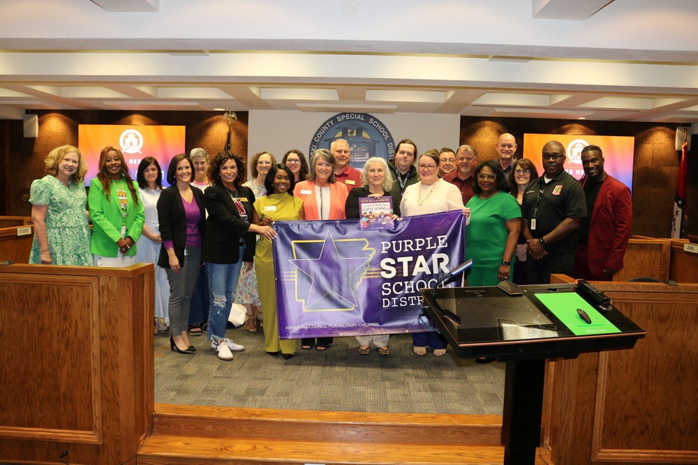 Group picture of PCSSD admins surrounding a Purple Star School District banner