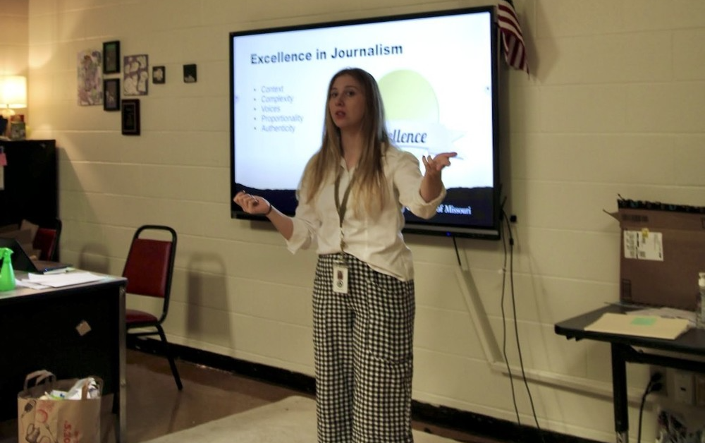 Rachel Farhat standing in front of a powerpoint presentation in a classroom teaching her journalism students excellence in journalism at Joe T. Robinson High School.