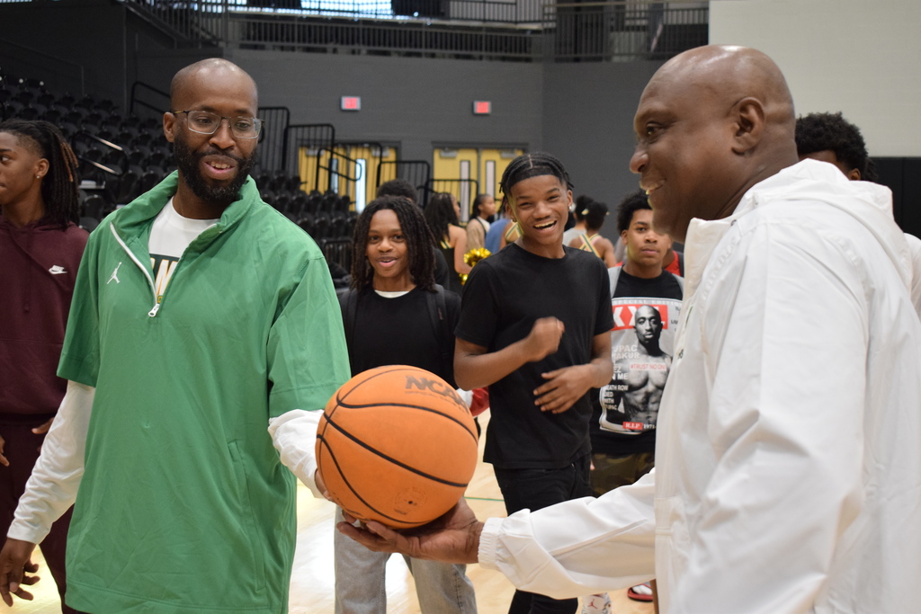 A basketball being handed to Coach Raymond A. Cooper. His team is smiling in the background.