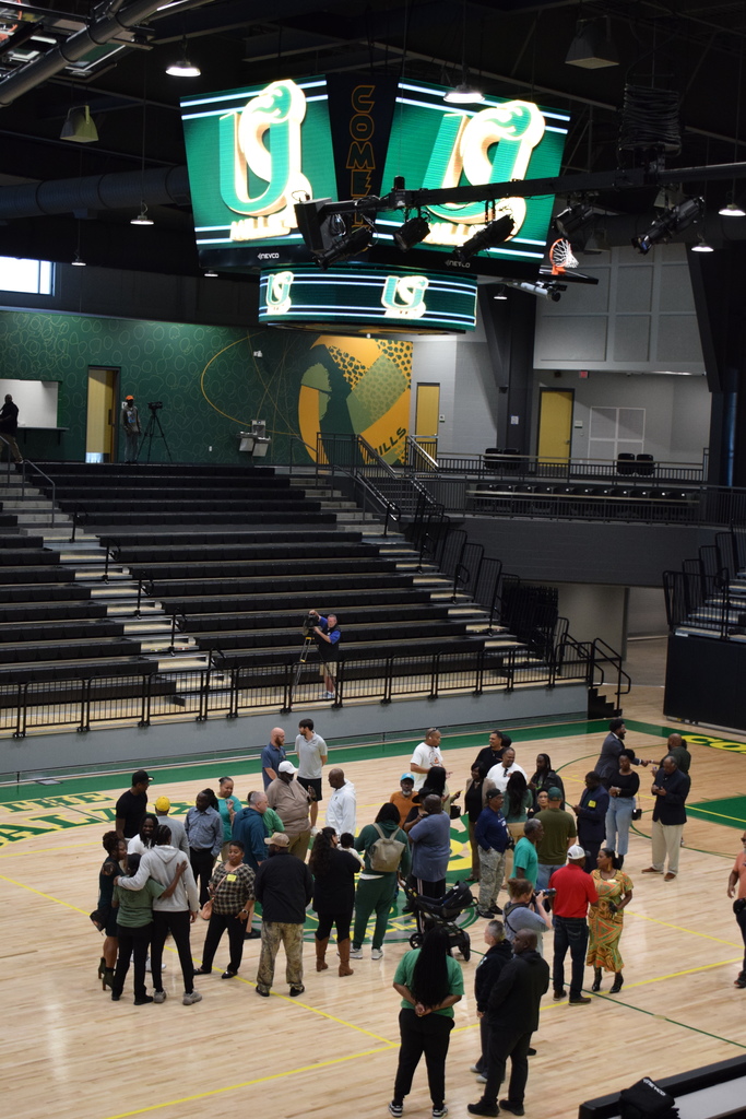 People gathered under an omnidirectional jumbotron that hangs above a basketball court