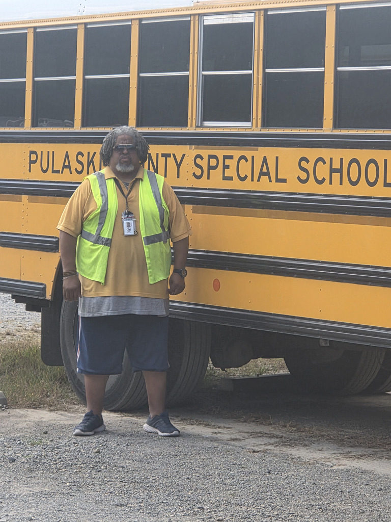 Reginald Jones -Robinson, a grey hearied man in a safety vest stands in front of a school bus with the text 'Pulaski County Special School District' on it.