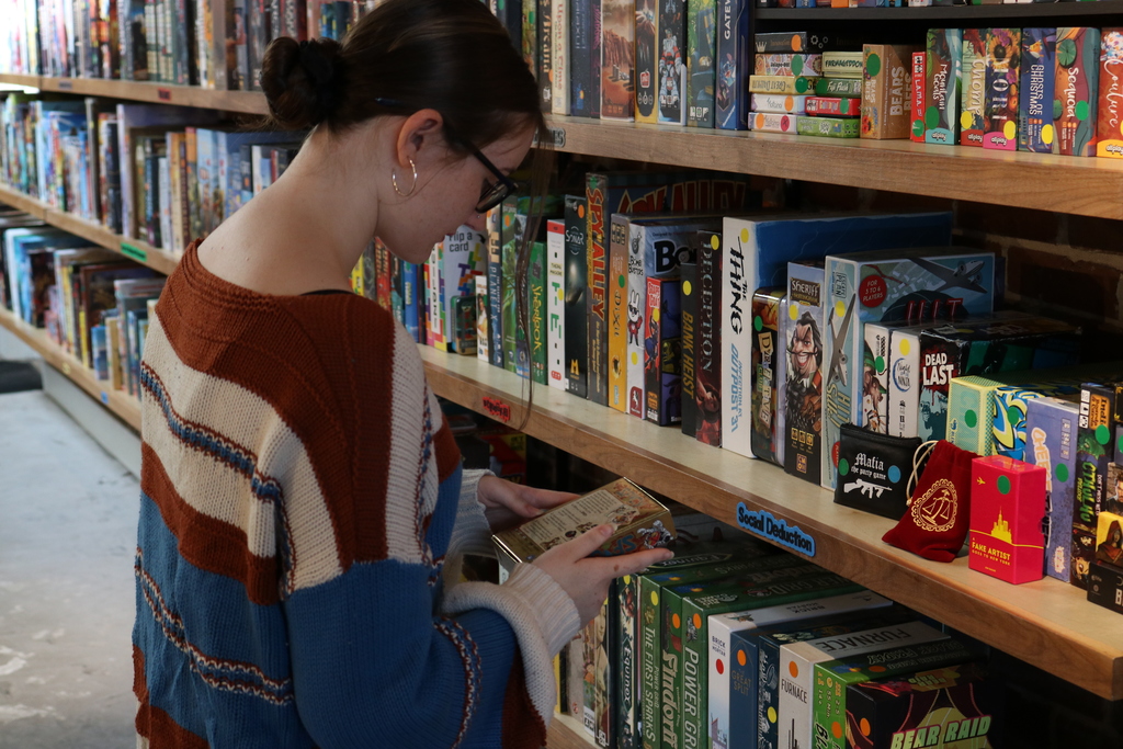 A person in a striped sweater browsing shelves full of games in a board game cafe.