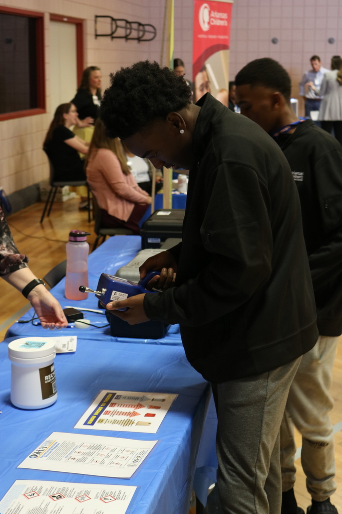 People at a booth looking at medical instruments and documents, with a display banner in the background.