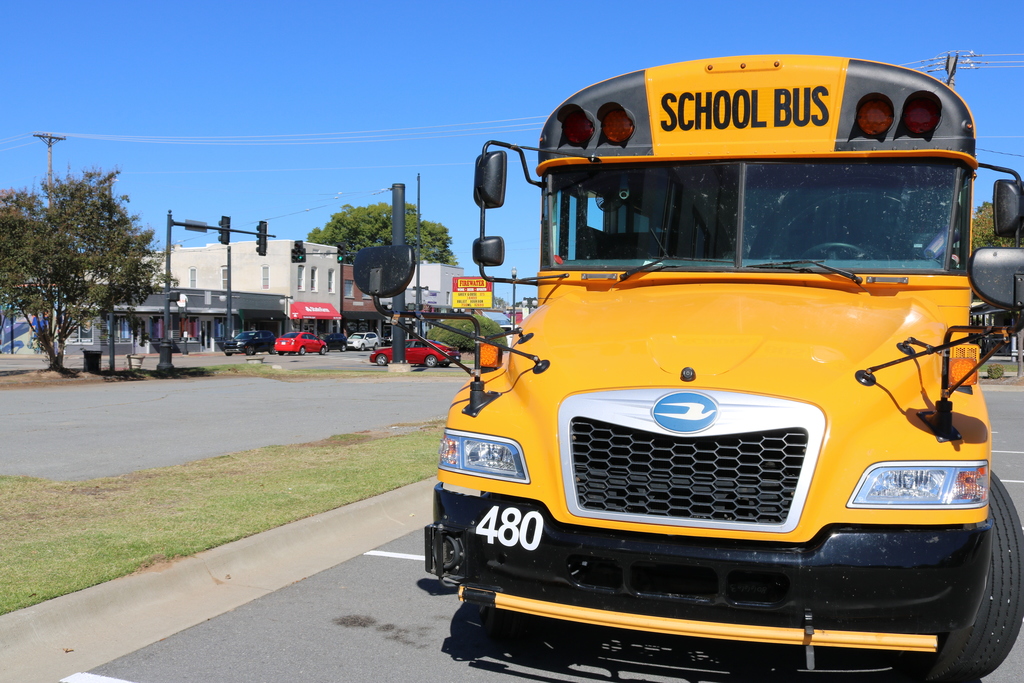 A yellow school bus parked on a city street with stop signs and traffic lights visible in the background.