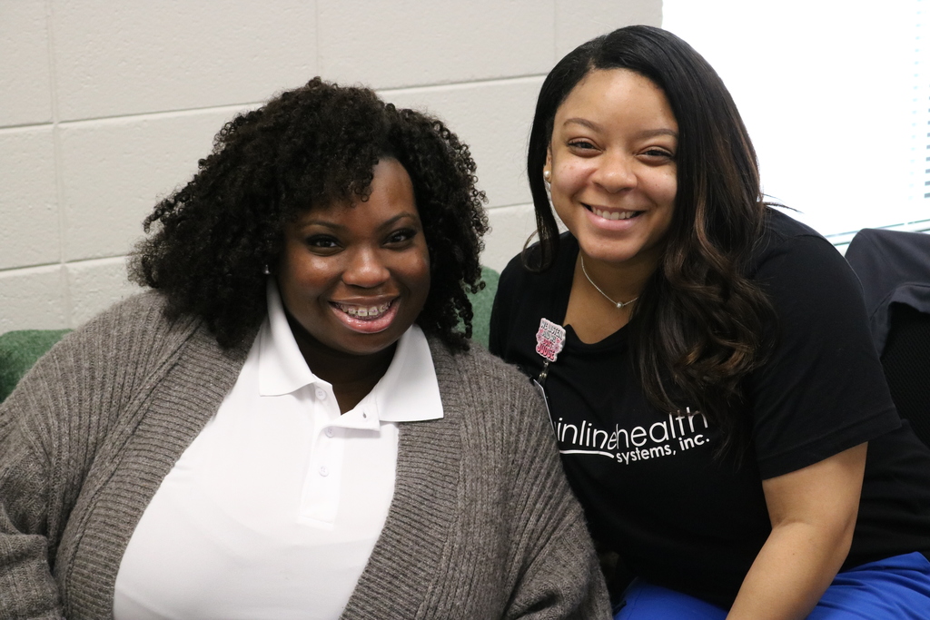 Two women with warm smiles sitting together, one with curly dark hair and the other with long dark hair.