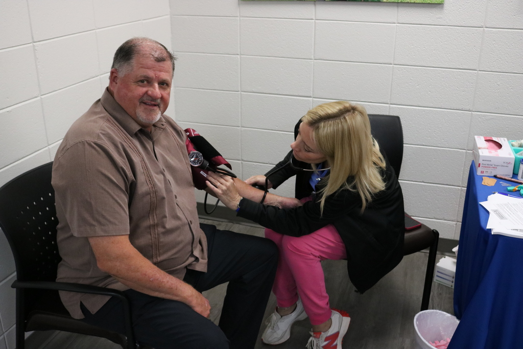 An older man in a button-up shirt sitting in a chair while a woman in a pink top attends to him.