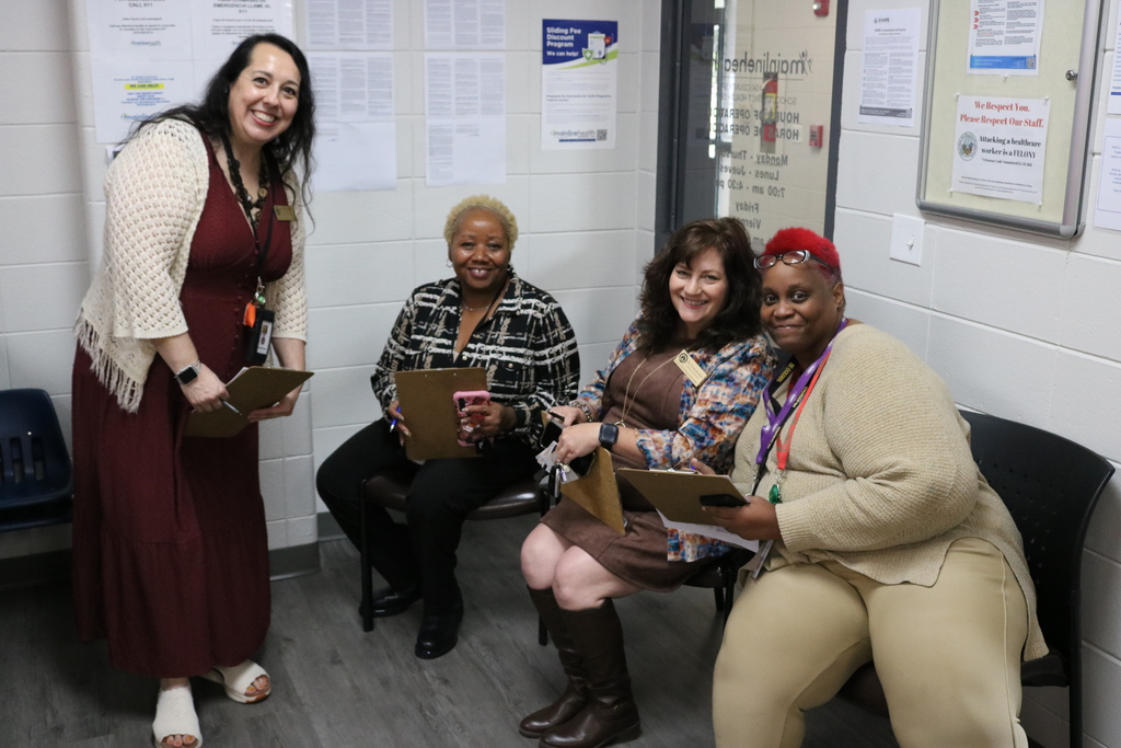 A group of four women of varying ages and ethnicities sitting together and looking at a tablet or document.