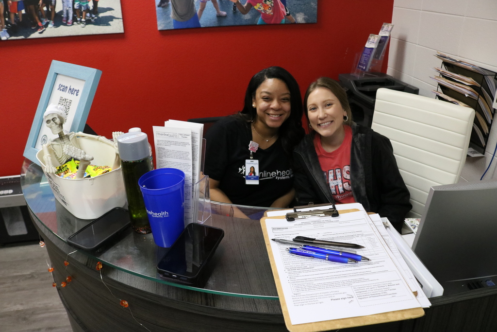 Two young women sitting at a desk, smiling and working on paperwork.