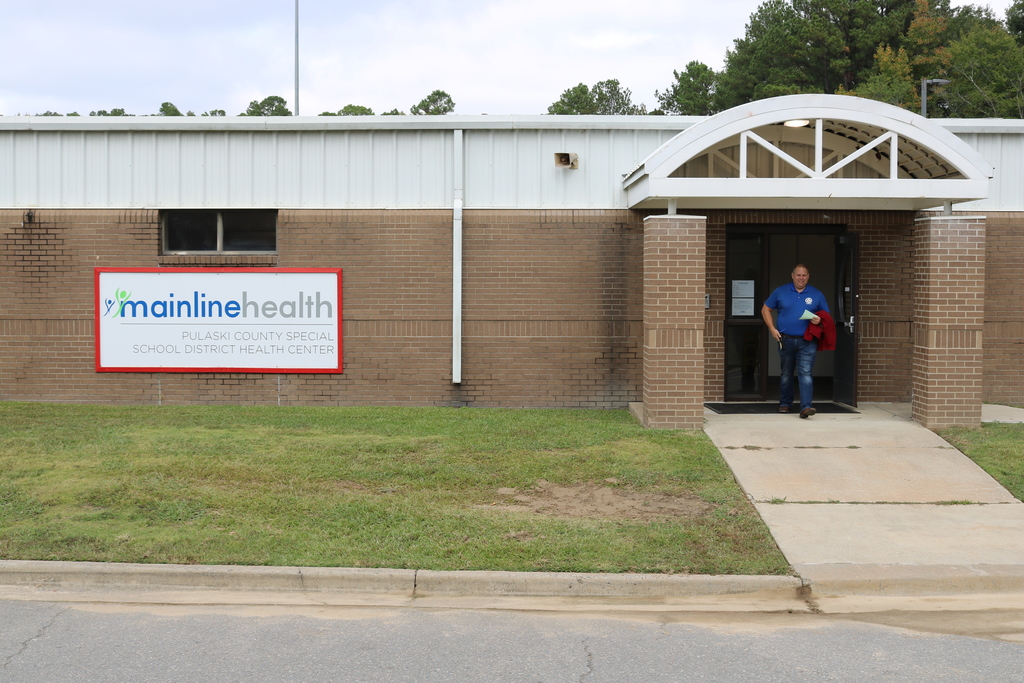 A brick building with a sign that says "Mainline Health". A person is standing in the doorway.