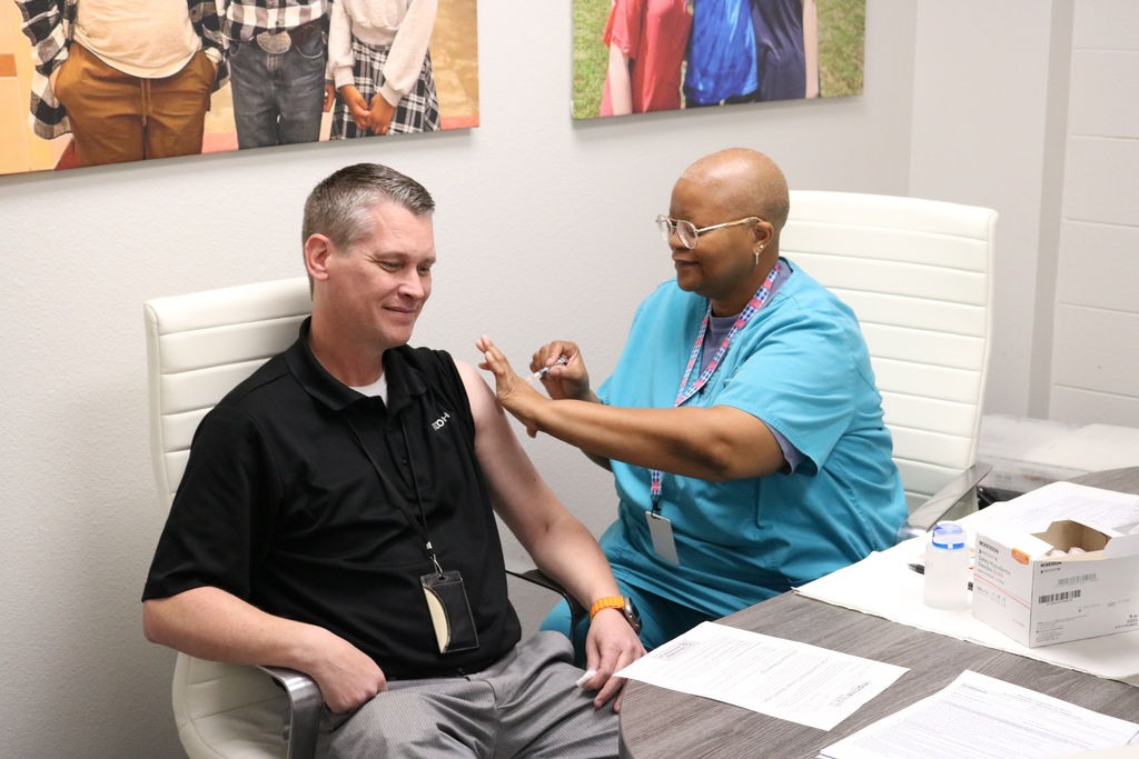 An older man in a button-up shirt sitting in a chair while a woman in a pink top attends to him.