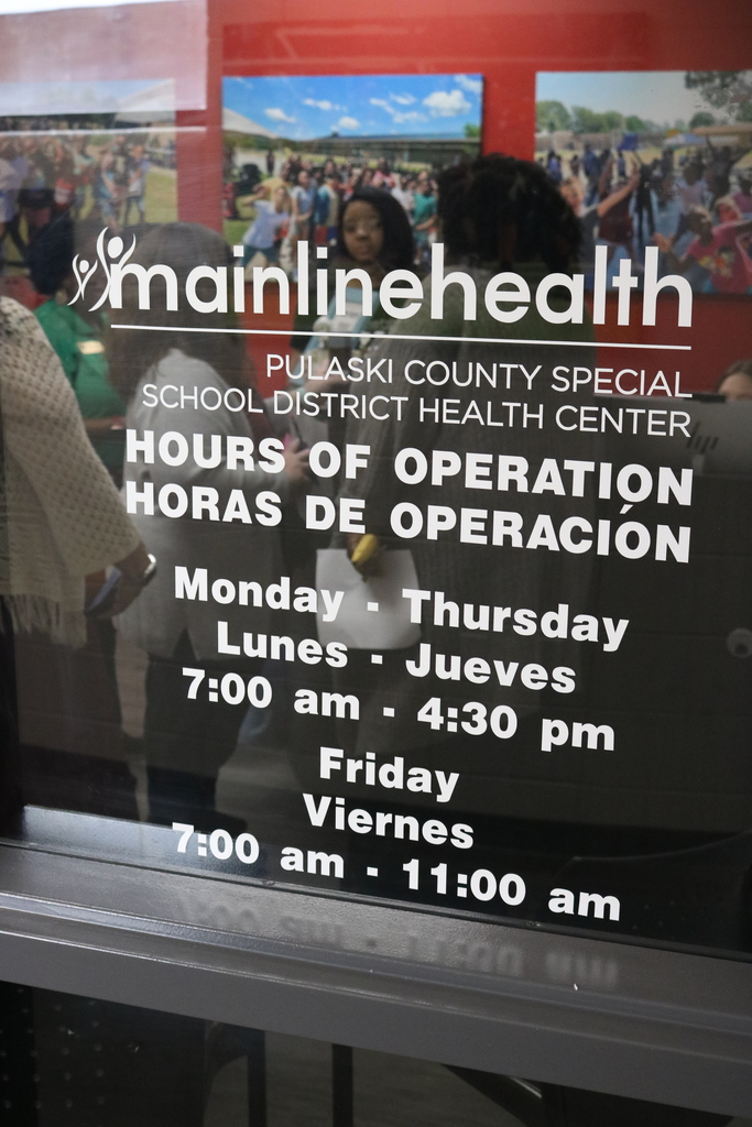 A sign displaying the hours of operation for the Pulaski County Special School District Health Center, operated by Mainline Health. The hours are listed in English and Spanish.