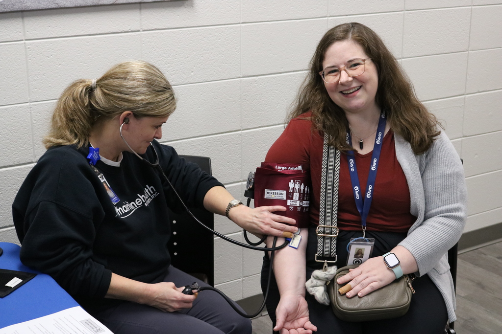 Two women sitting at a table, one wearing a Bodewell nametag and the other wearing a red shirt, engaged in conversation.