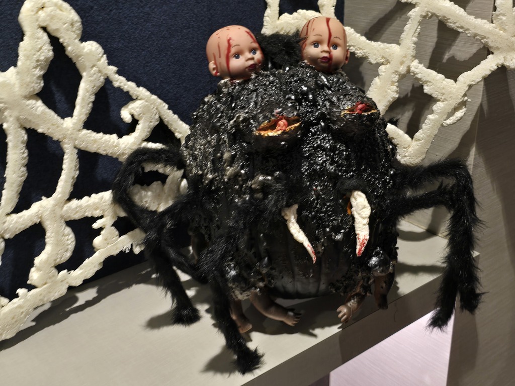 Creepy spider-like creature with two doll heads attached to its black and furry body.