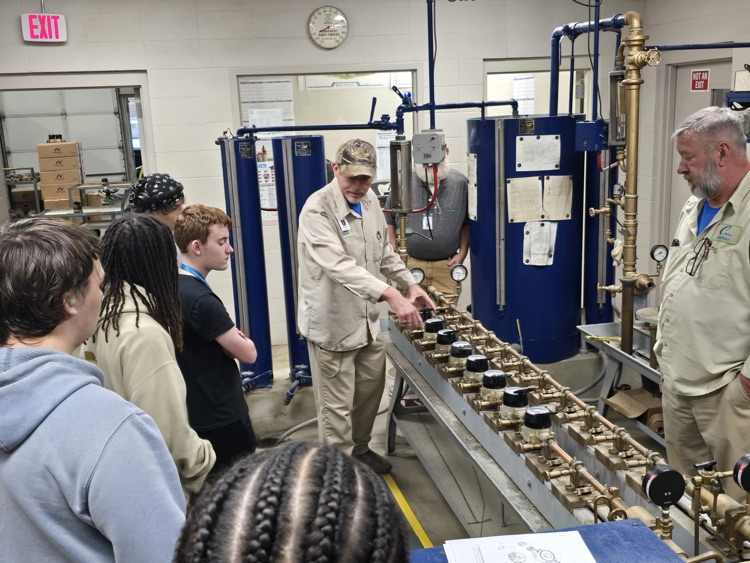 Group of people in a workshop examining car parts on a workbench.