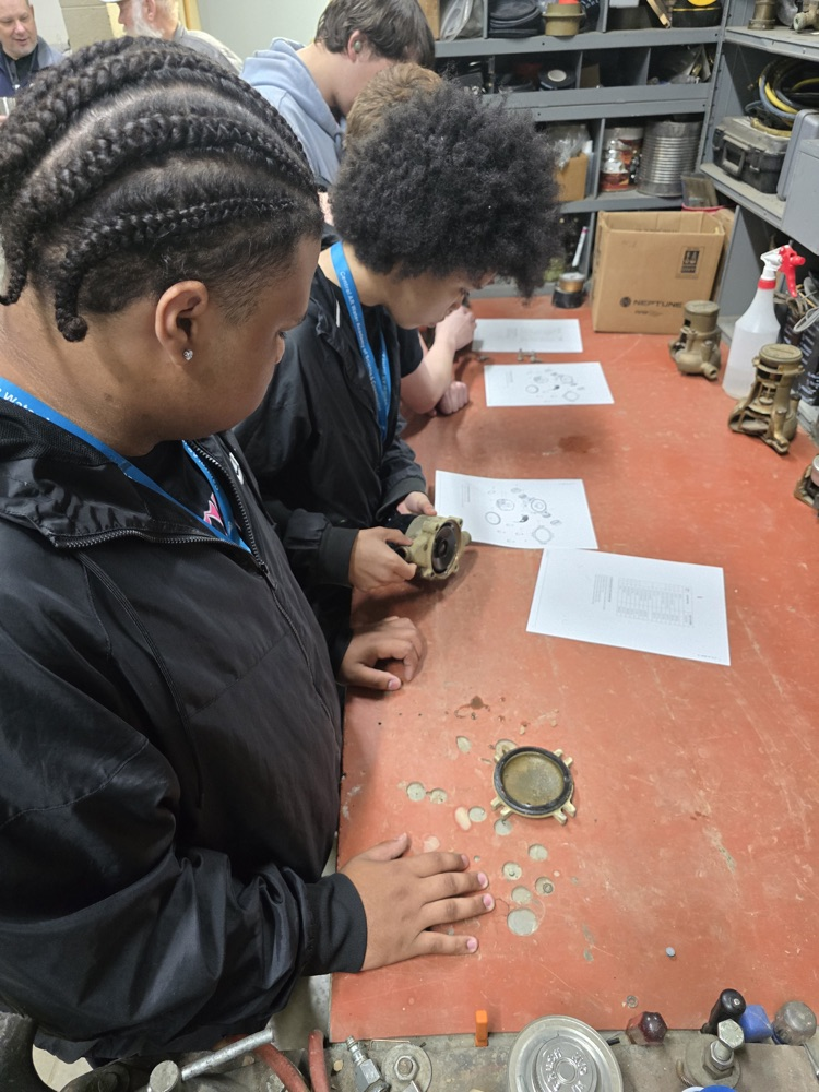 Two students with braided hairstyles sitting at a table, examining objects and documents.
