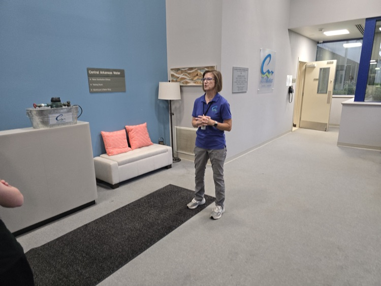 A man in a blue shirt and jeans standing in a modern, minimalist office lobby with a sofa, artwork, and signs on the walls.
