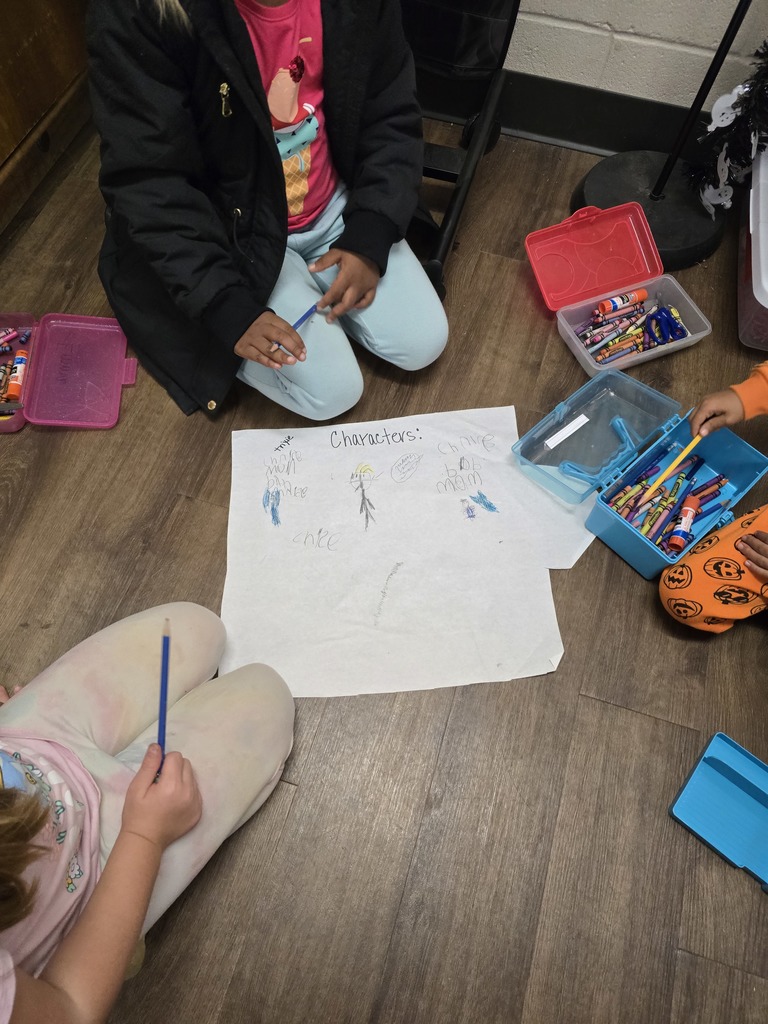 Three children sitting on the floor, surrounding art supplies and a paper drawing.