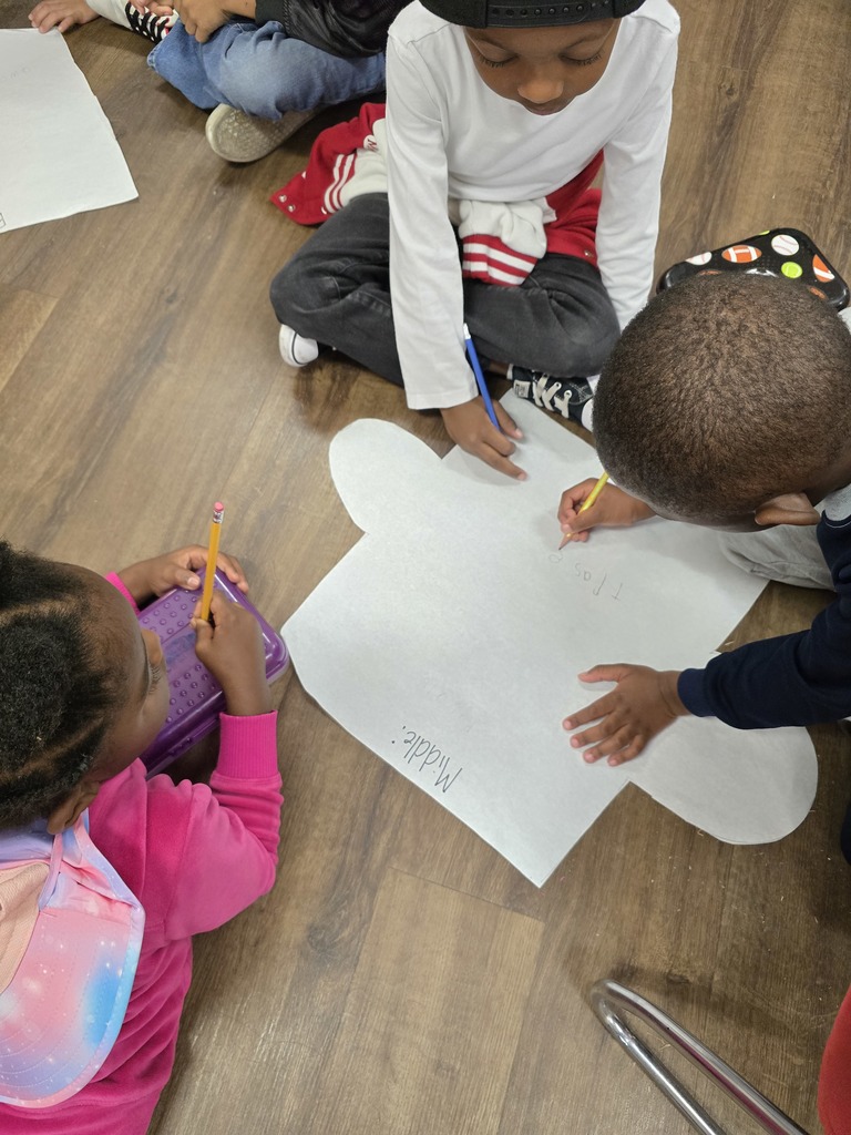 Several young children seated on the floor, drawing and coloring on large sheets of paper shaped like puzzle pieces with crayons and markers.