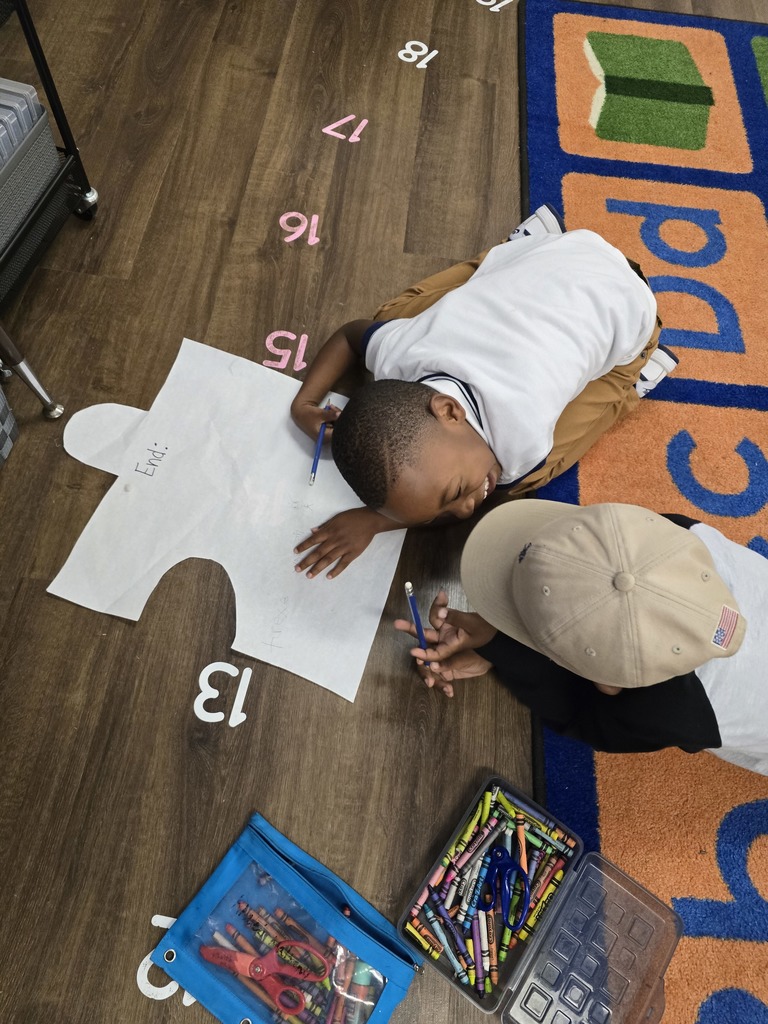 A young child lying on the floor, surrounded by educational materials such as numbers, shapes, and colored pencils. Another kid is smiling at him.