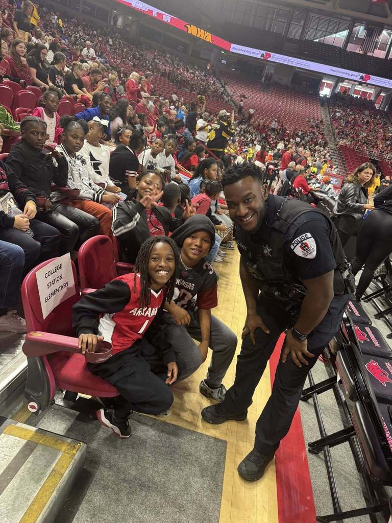 College Station studenst at University of Arkansas basketball game smiling with police officer