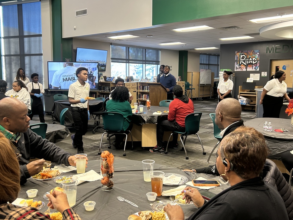 Group image of adults eating while guest speaker talks