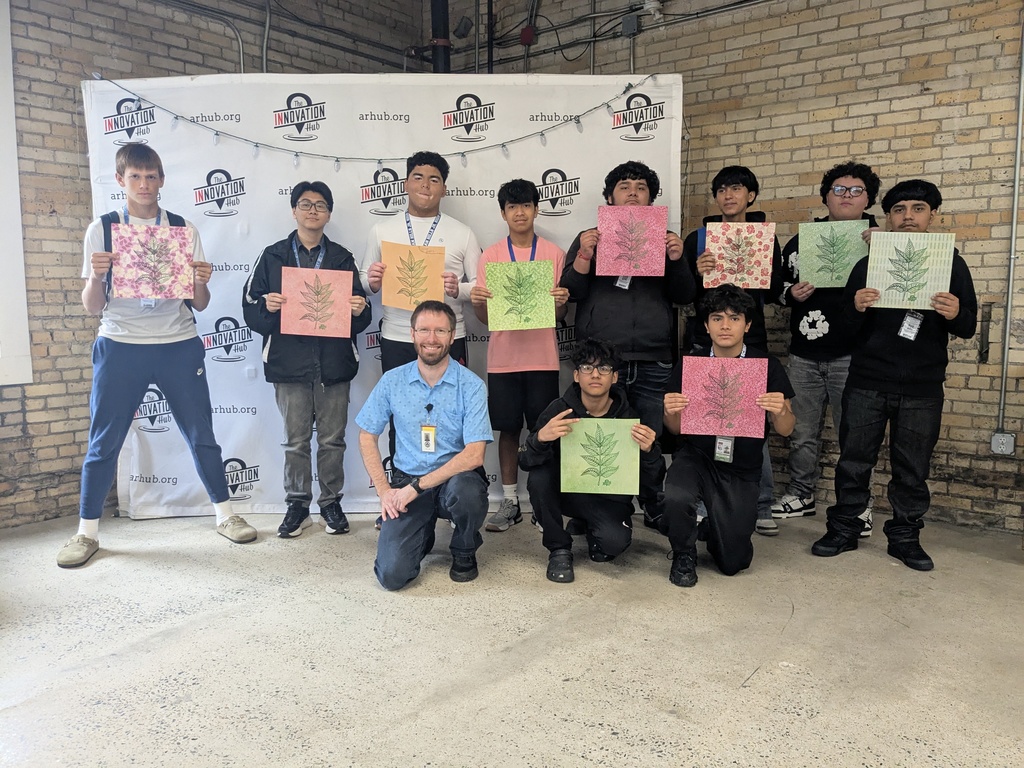 A group of children in casual attire posing for a photo in front of a brick wall with signage.