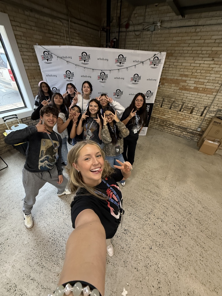 Group photo of young people posing in front of a wall with branded signage and logos.