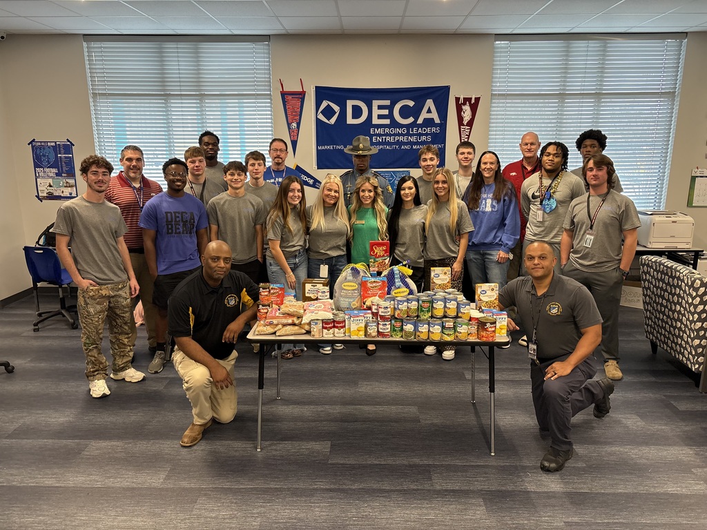 DECA students and Arkansas State Troopers stand  around a table full of donated food. They are smiling at the camera.