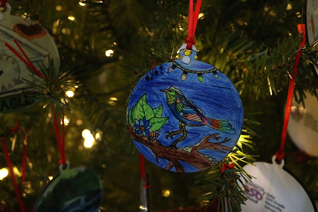 An ornament hanging from a Christmas tree. It has a blue bird on it.
