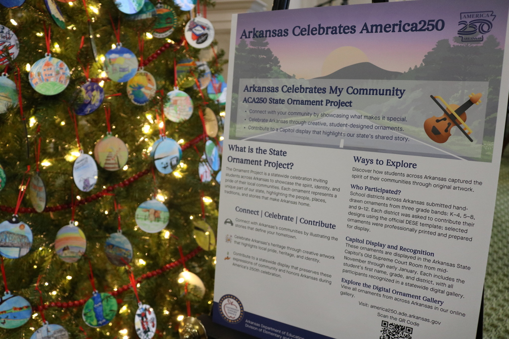 A sign display next to a Christmas tree. It is for the ACA250 State ornament Project