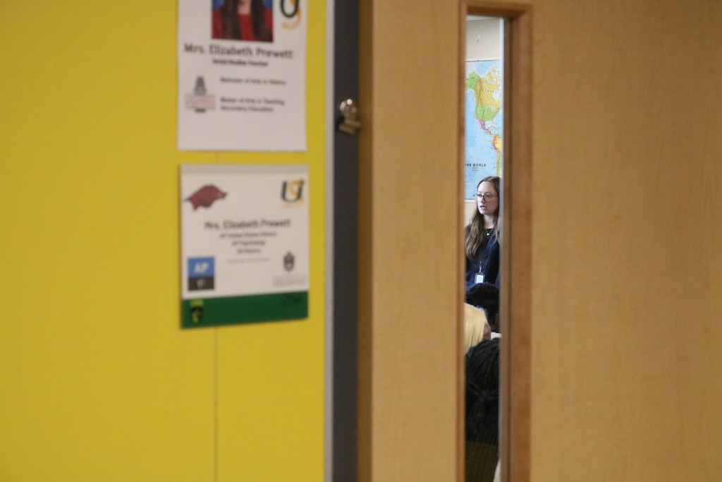 Yellow walls with student achievement posters. Person partially visible in doorway.