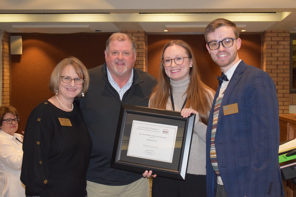 Four people smiling and holding a framed certificate in a gathering.