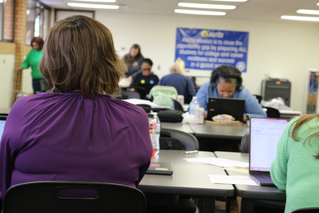 People sitting at desks in a classroom-like setting, with posters and signs on the walls.