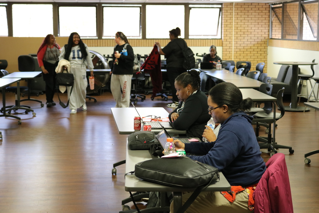 Classroom with adults working at desks, some standing in groups.