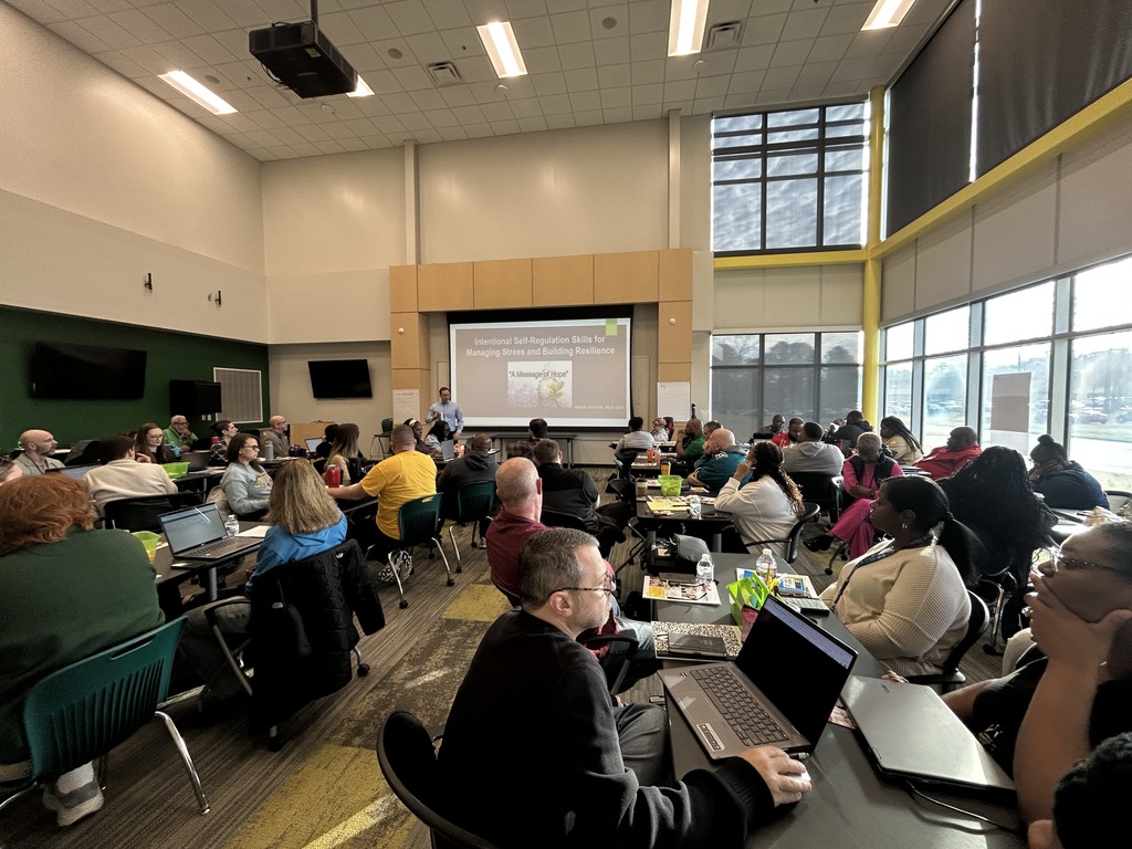 Full room of teachers receiving professional development. A presentation is projected saying, "Self-Regulation Skills for Managing Stress and Building Resilience"